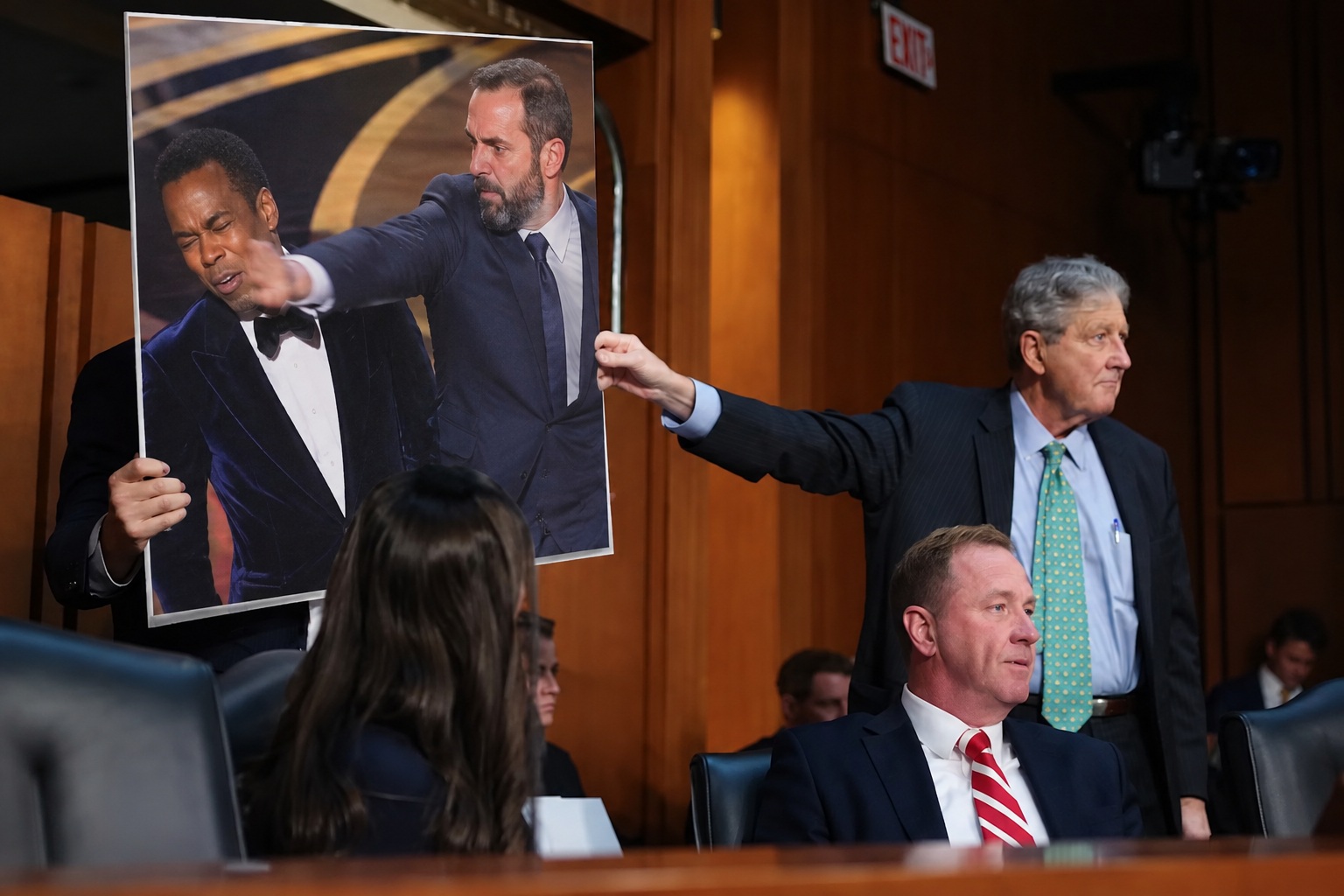 A senator presents a poster depicting a man striking comedian Chris Rock onstage.